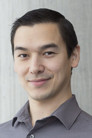 Headshot of Kevin Connors. Kevin has short dark hair, is wearing a grey button down shirt, and is smiling at the camera.